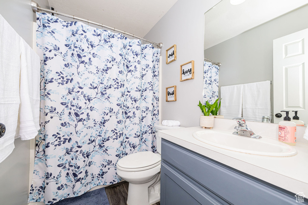 Full bath with toilet, a shower with curtain, vanity, and wood finished floors