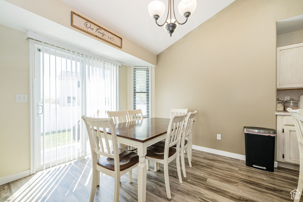 Dining area with lofted ceiling, a notable chandelier, wood finished floors, and baseboards