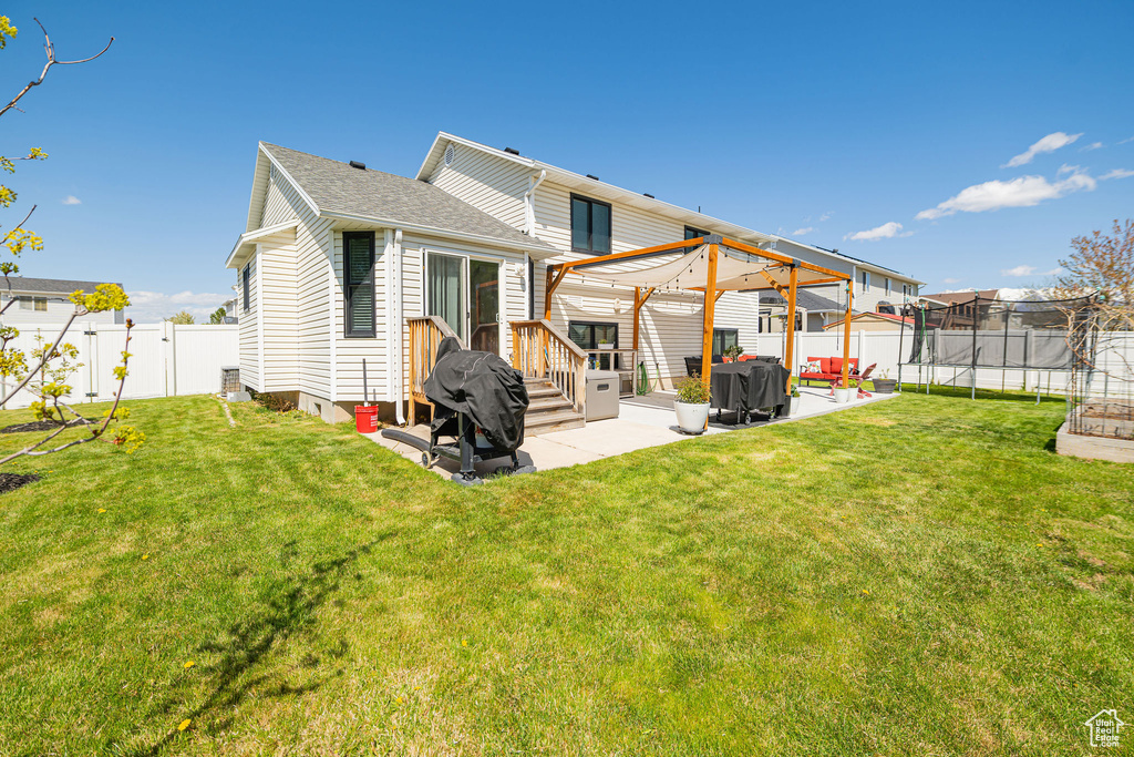 Rear view of house featuring a patio area, a trampoline, a lawn, a fenced backyard, and roof with shingles
