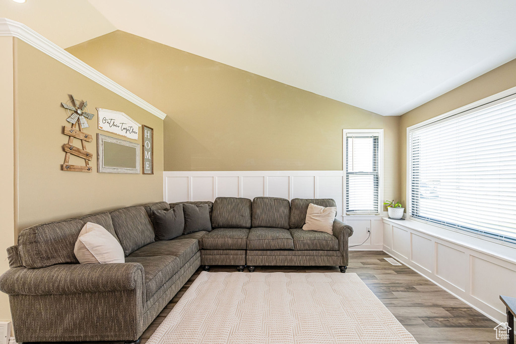 Living area with vaulted ceiling, wood finished floors, a wainscoted wall, and a decorative wall