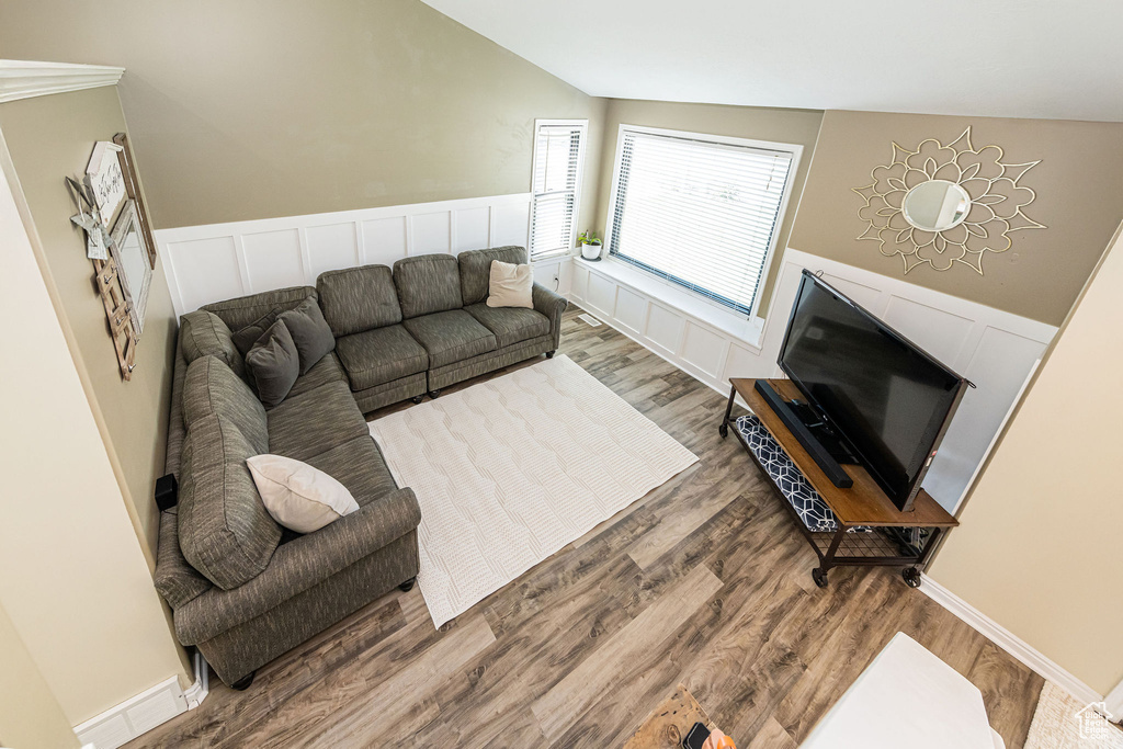Living area featuring vaulted ceiling, wood finished floors, and a wainscoted wall