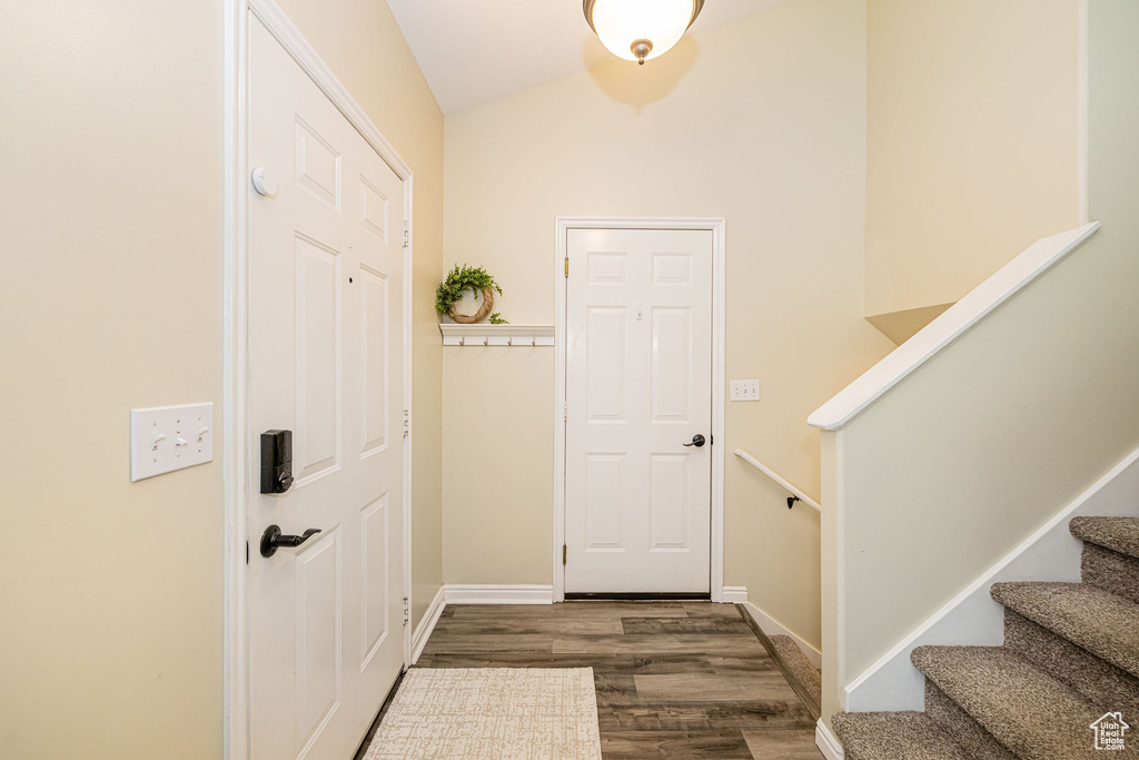 Foyer featuring stairs, lofted ceiling, dark wood-type flooring, and baseboards