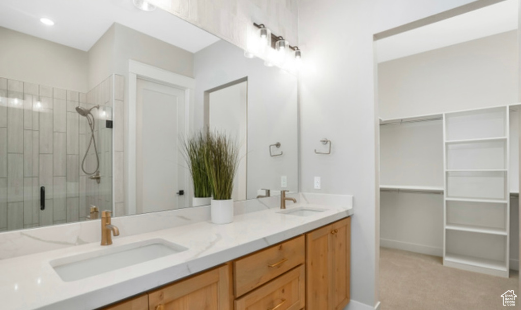 Full bath featuring double vanity, a spacious closet, a stall shower, and a sink