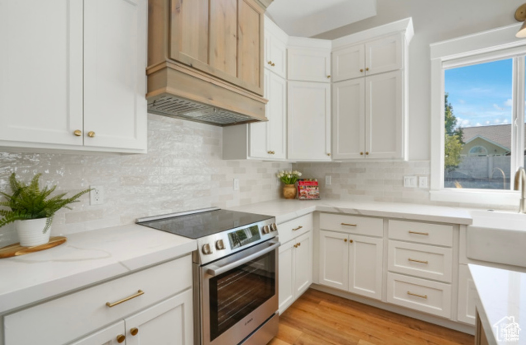 Kitchen with light stone counters, a sink, stainless steel electric stove, white cabinets, and backsplash