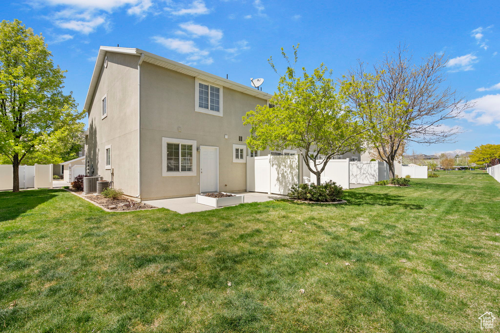 Back of property with a fenced backyard, stucco siding, a patio, central AC unit, and a lawn