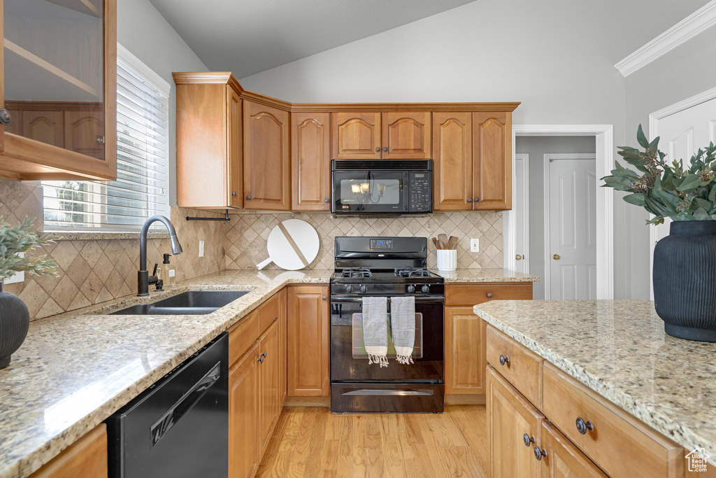 Kitchen with vaulted ceiling, a sink, black appliances, light wood-style floors, and light stone countertops
