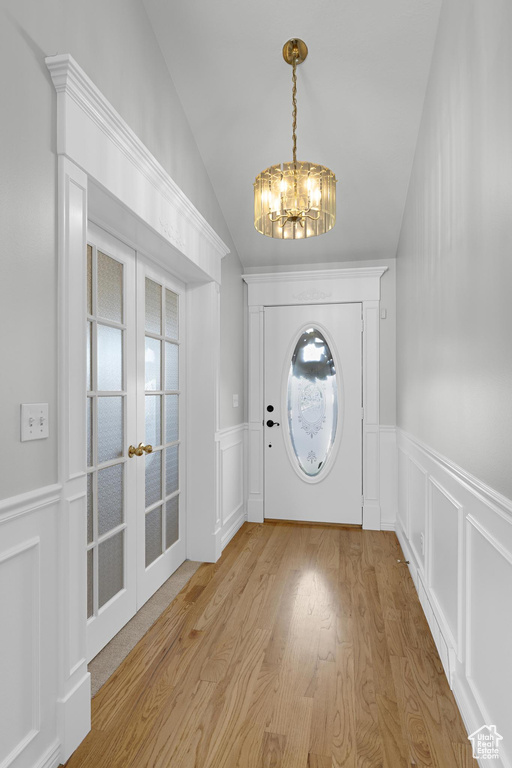 Entrance foyer featuring vaulted ceiling, wainscoting, a chandelier, light wood-type flooring, and french doors