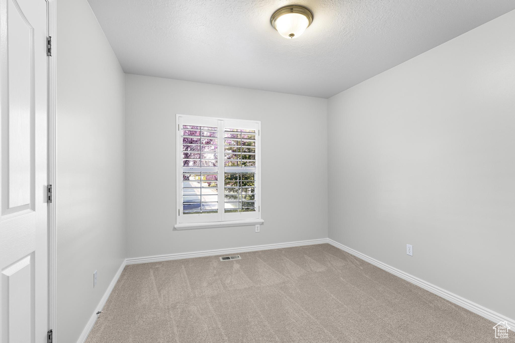 Carpeted spare room with baseboards, a textured ceiling, and visible vents
