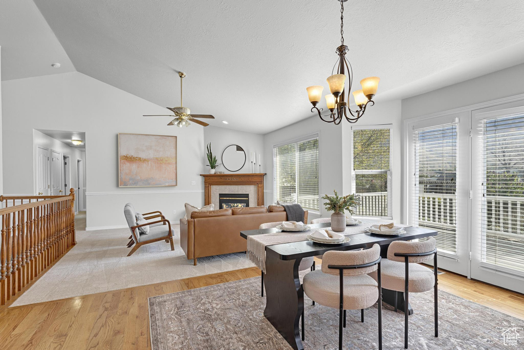 Dining room featuring ceiling fan with notable chandelier, a tiled fireplace, vaulted ceiling, and light wood finished floors