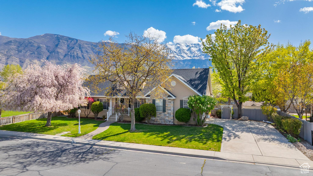 View of front of house featuring a front lawn, a mountain view, stone siding, concrete driveway, and fence