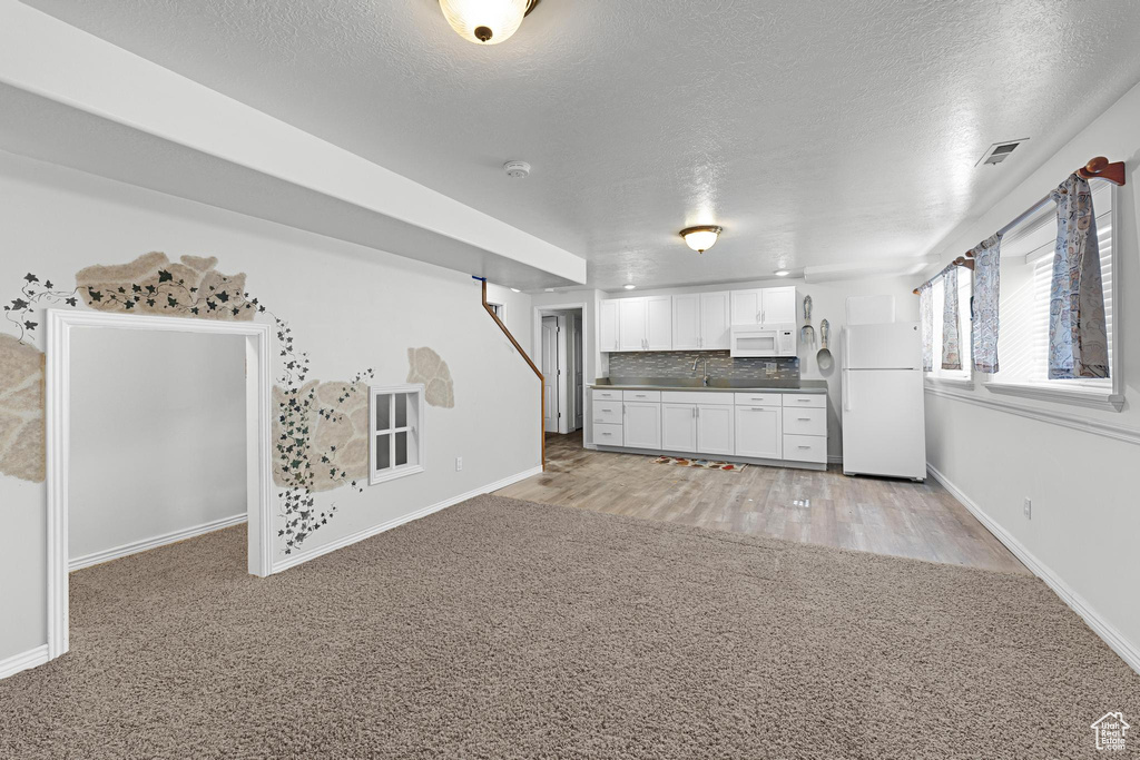 Unfurnished living room featuring a textured ceiling, visible vents, baseboards, and light carpet