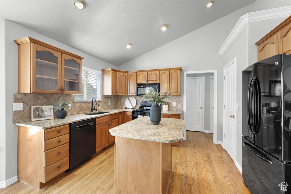 Kitchen with a sink, light stone countertops, decorative backsplash, black appliances, and glass insert cabinets