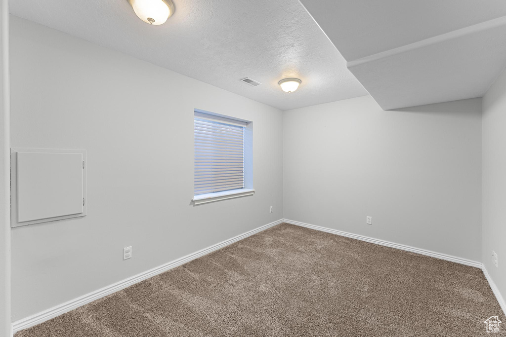 Carpeted spare room with baseboards, a textured ceiling, and visible vents