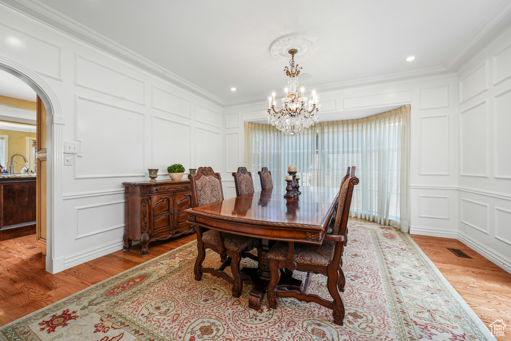 Dining room with a decorative wall, light wood-type flooring, a chandelier, arched walkways, and crown molding
