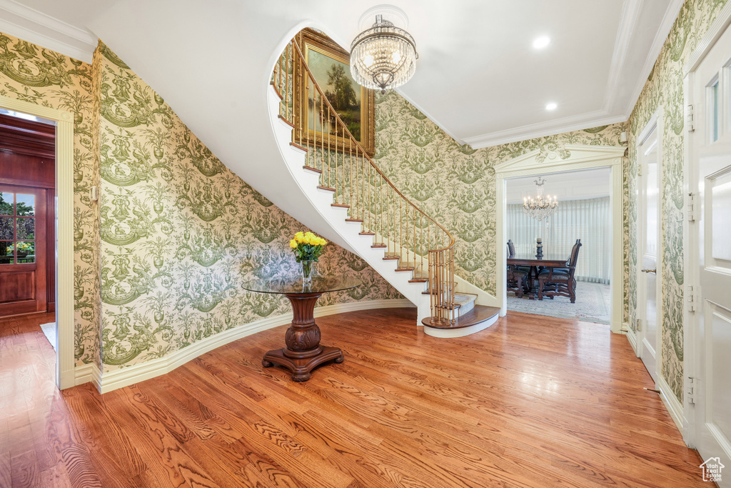 Entrance foyer featuring a chandelier, wallpapered walls, stairway, wood finished floors, and ornamental molding