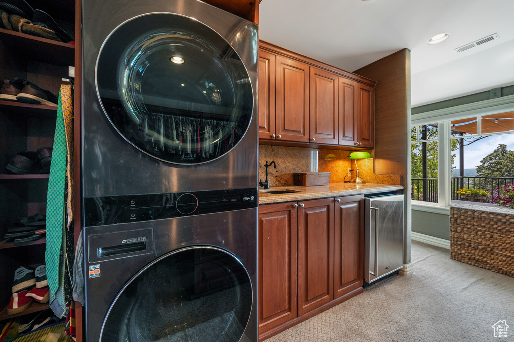 Laundry room featuring stacked washer / dryer, light colored carpet, cabinet space, and wet bar