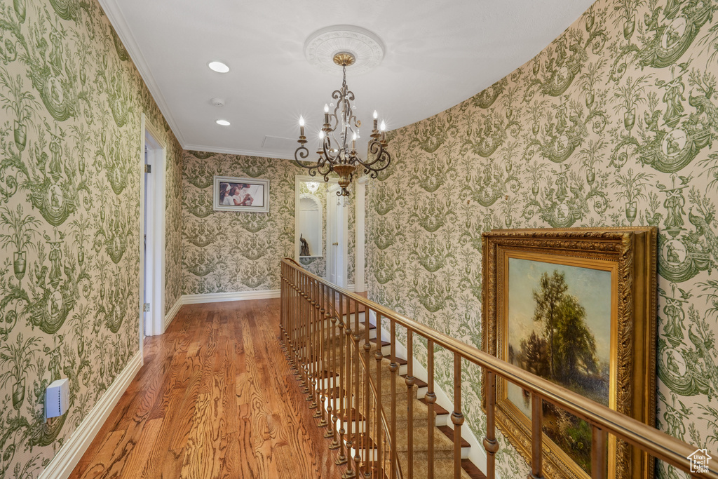 Hall with wood finished floors, wallpapered walls, a chandelier, ornamental molding, and recessed lighting