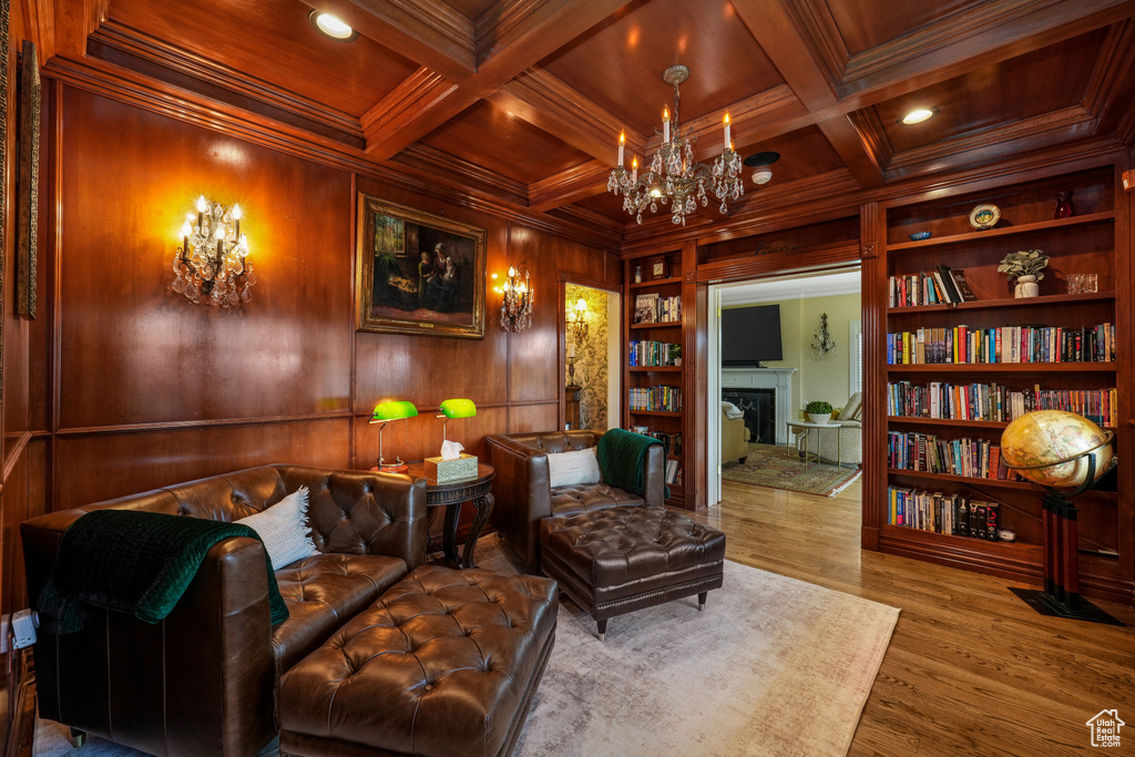Sitting room with a fireplace, built in shelves, a wood ceiling with exposed beams, wooden walls, and ornamental molding