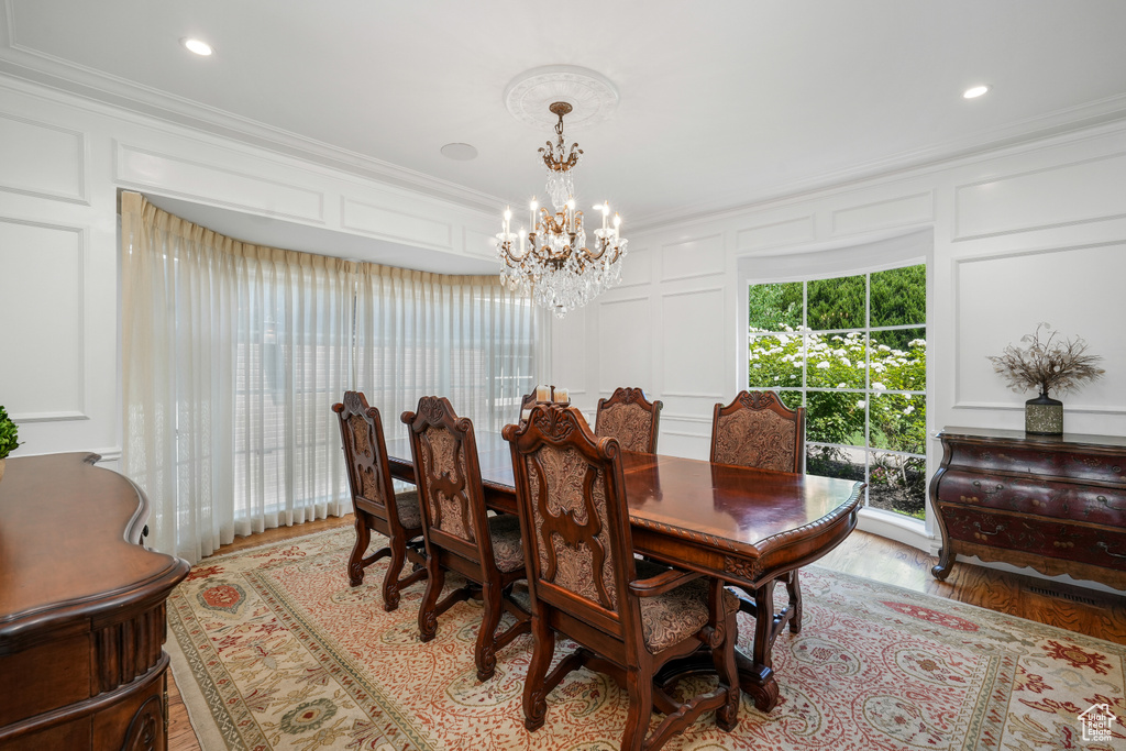 Dining space featuring a decorative wall, a chandelier, ornamental molding, light wood-type flooring, and recessed lighting