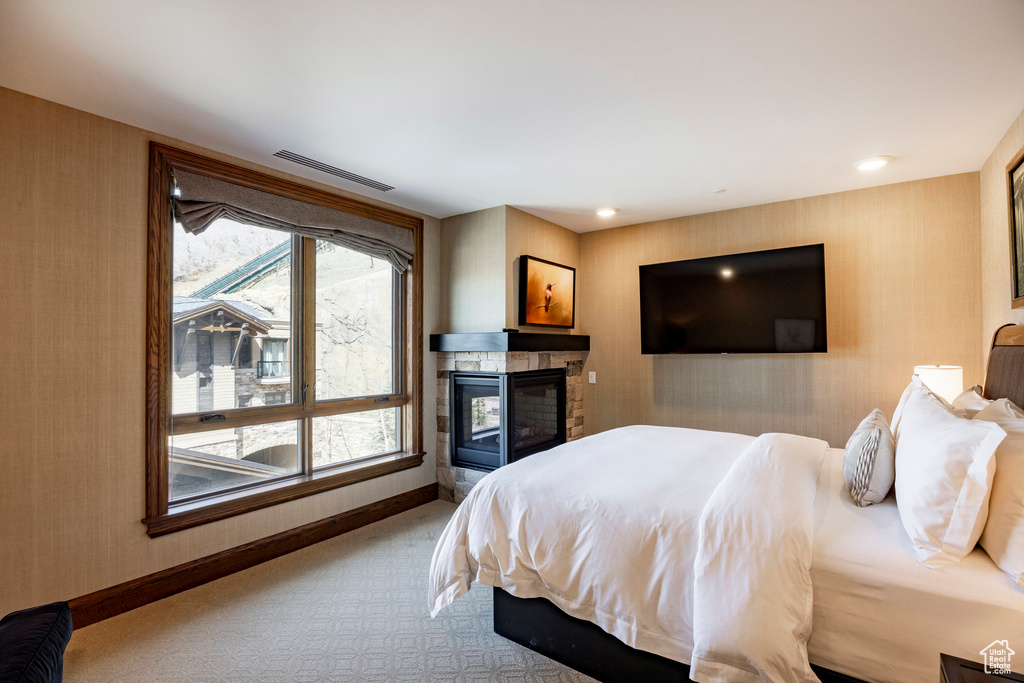 Carpeted bedroom with wallpapered walls, baseboards, visible vents, and a tile fireplace