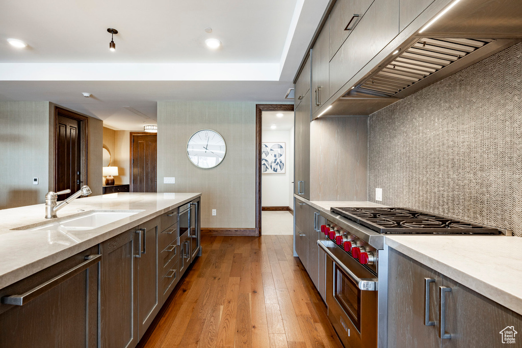 Kitchen with light stone counters, a sink, high end range, light wood-style floors, and range hood