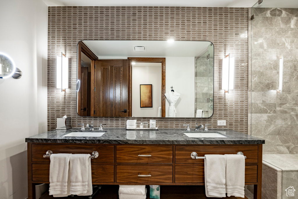 Full bath with backsplash, double vanity, tiled shower, and a sink
