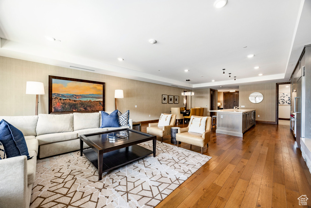 Living room featuring wallpapered walls, light wood-style floors, a raised ceiling, and recessed lighting