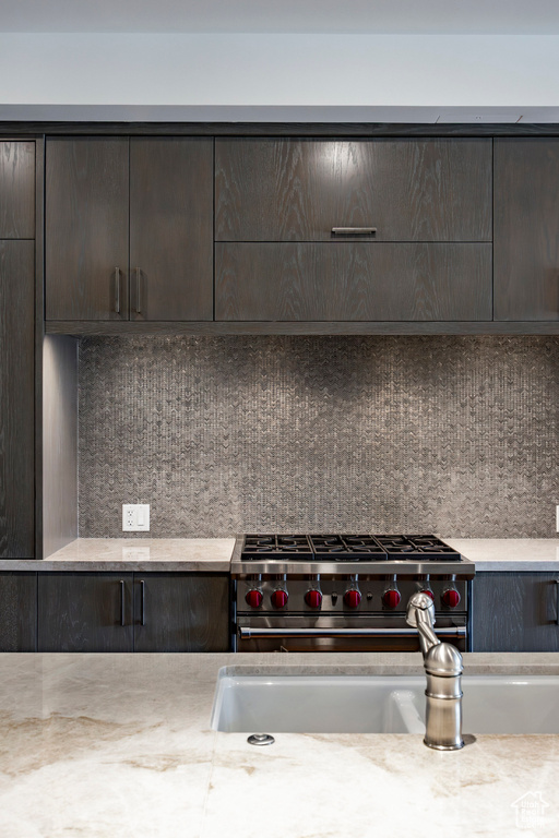 Interior space featuring high end stainless steel range, a sink, dark brown cabinetry, backsplash, and light countertops