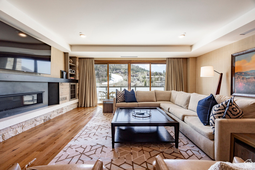 Living room featuring visible vents, built in shelves, wood finished floors, a stone fireplace, and a raised ceiling