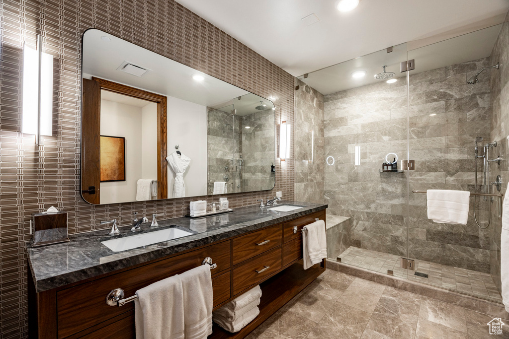 Bathroom featuring a shower stall, tile walls, double vanity, and a sink