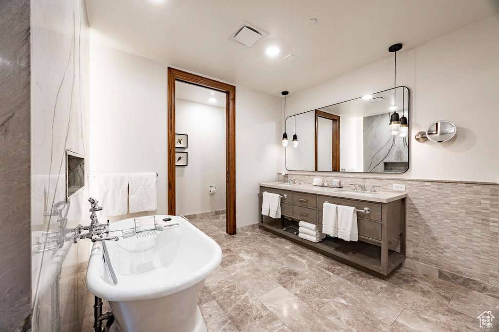 Full bath featuring double vanity, tile walls, a soaking tub, and a sink