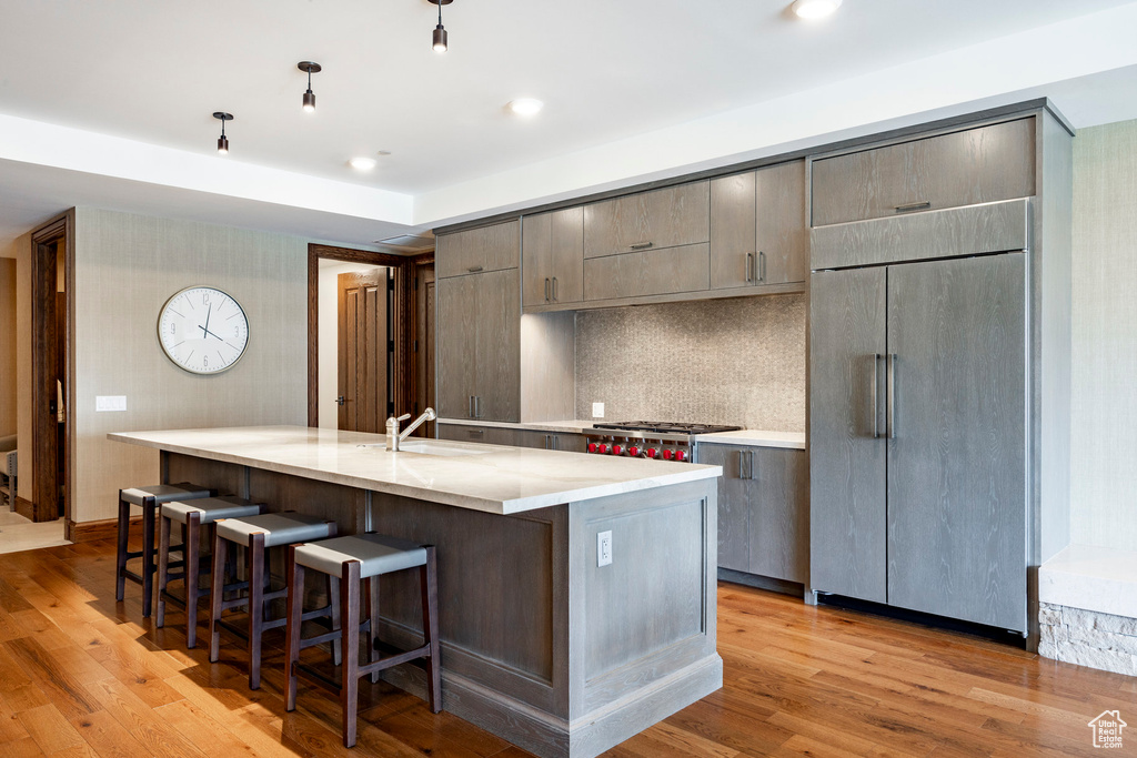 Kitchen featuring light wood finished floors, an island with sink, a sink, built in fridge, and a kitchen bar