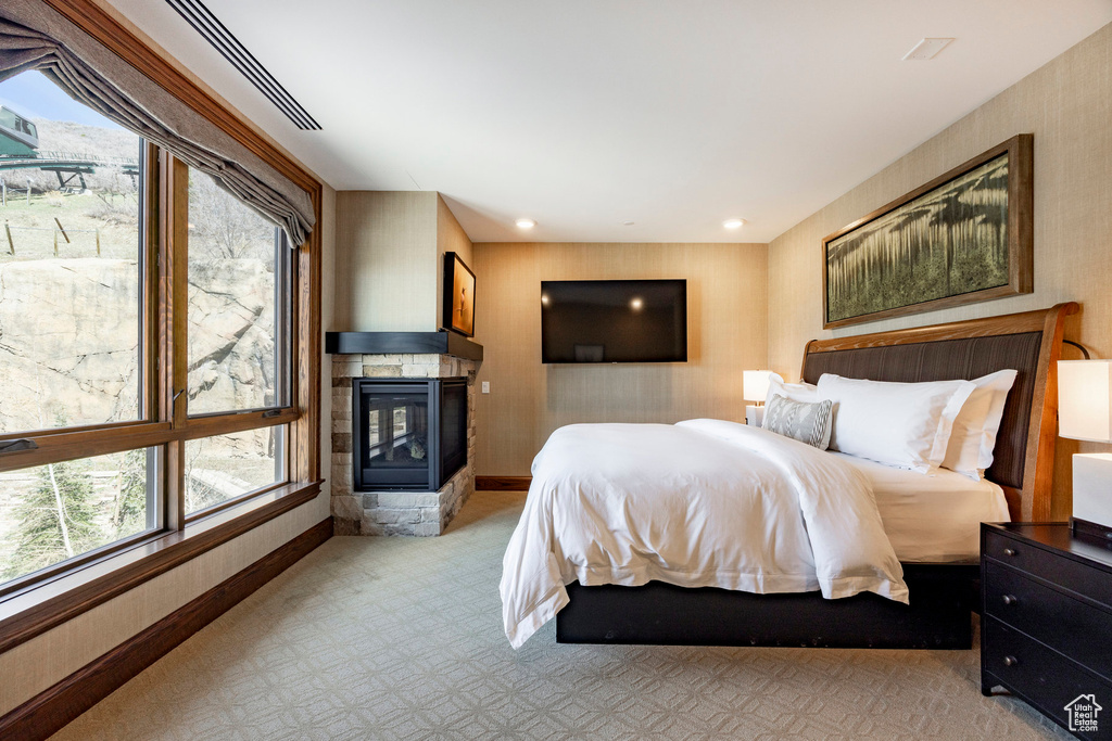 Bedroom with light carpet, wallpapered walls, multiple windows, and a multi sided fireplace