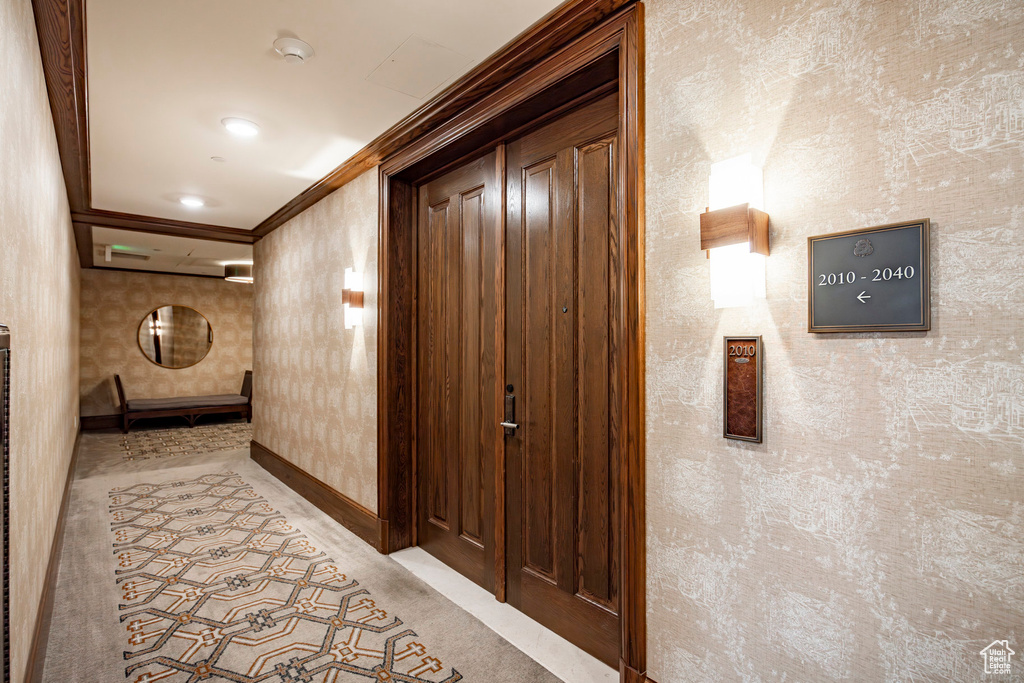 Hall featuring baseboards, crown molding, wallpapered walls, and carpet