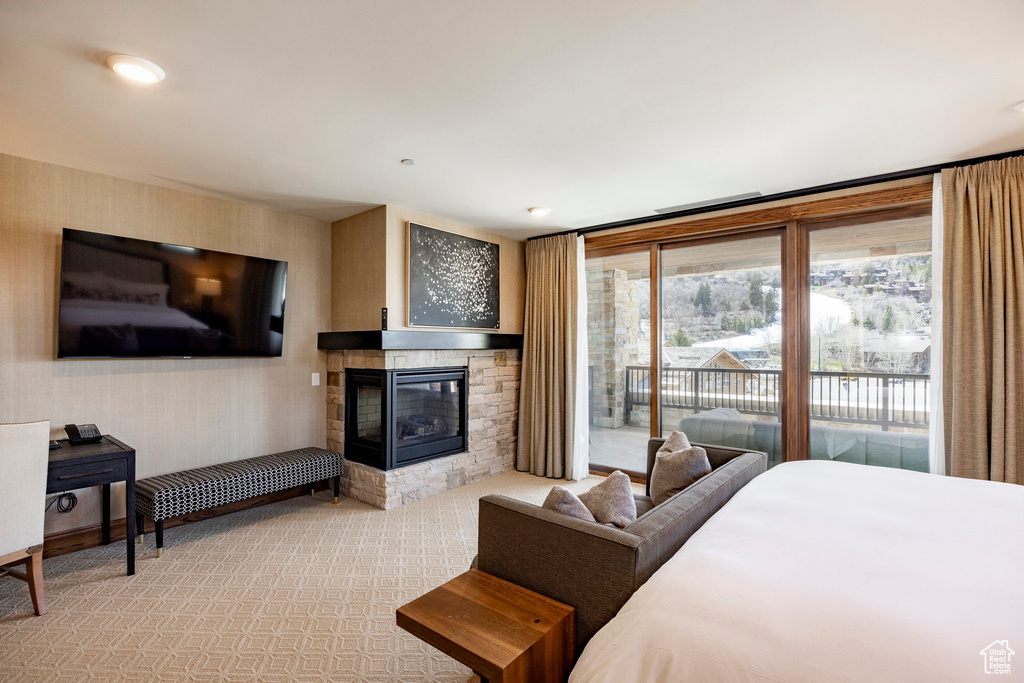 Bedroom featuring a stone fireplace, light colored carpet, and access to exterior