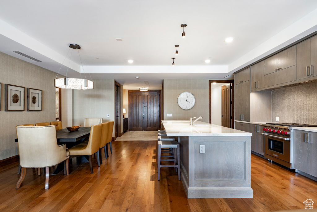 Kitchen featuring light wood finished floors, light countertops, luxury range, and an island with sink