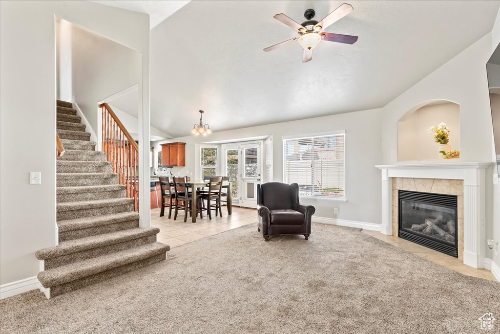 Living room featuring light carpet, vaulted ceiling, ceiling fan with notable chandelier, stairs, and a tile fireplace