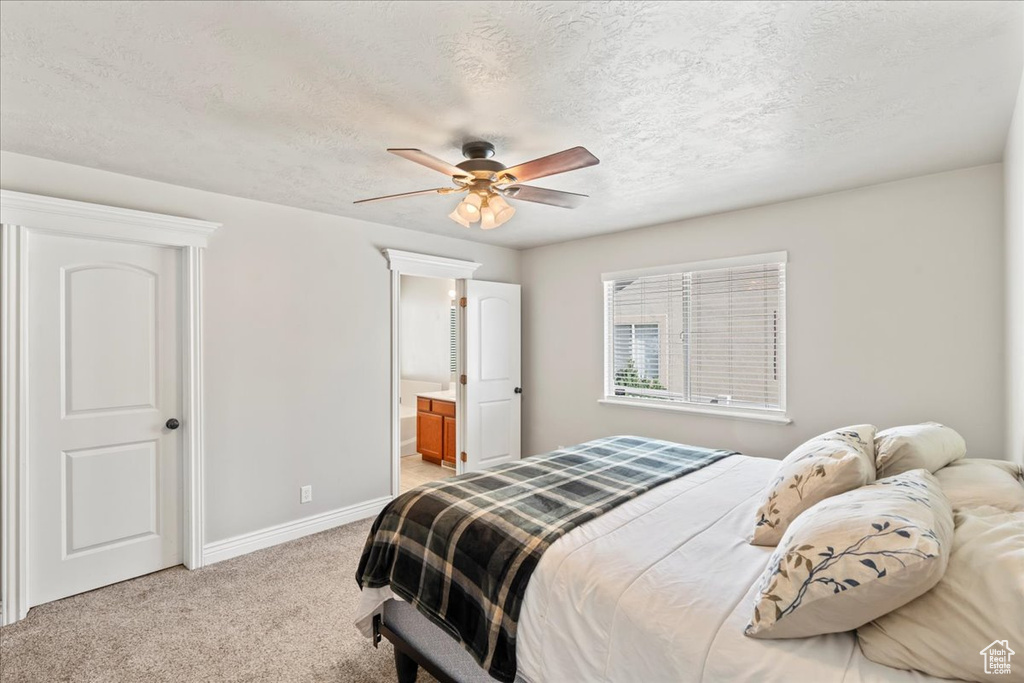 Bedroom featuring a textured ceiling, baseboards, light colored carpet, a ceiling fan, and ensuite bath
