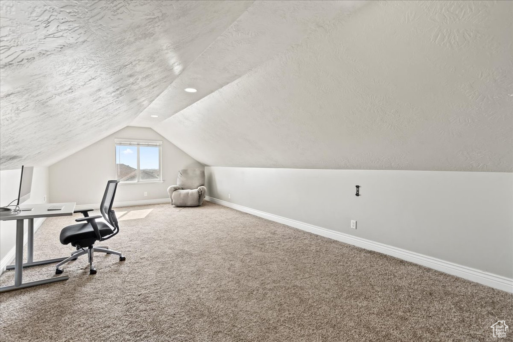 Unfurnished office with vaulted ceiling, baseboards, a textured ceiling, and carpet floors