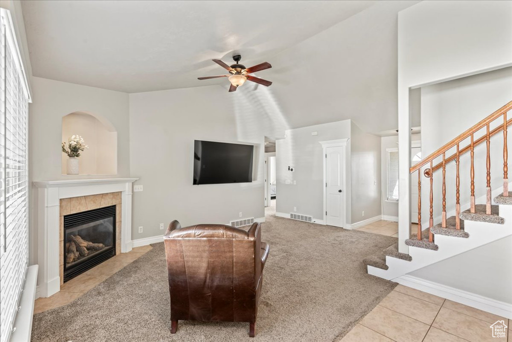 Carpeted living area with tile patterned flooring, visible vents, a ceiling fan, a fireplace, and stairs