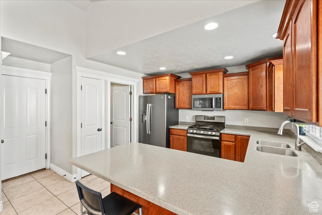 Kitchen with light countertops, light tile patterned floors, a sink, a peninsula, and appliances with stainless steel finishes