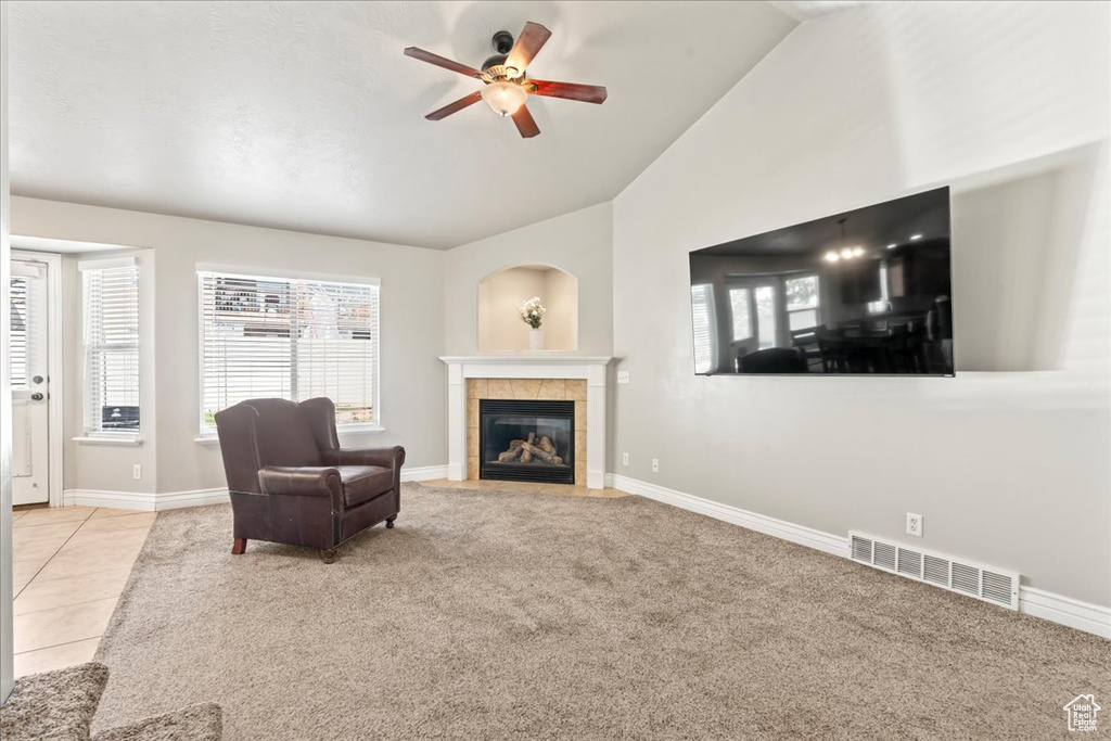 Carpeted living area featuring plenty of natural light, a tiled fireplace, vaulted ceiling, visible vents, and a ceiling fan