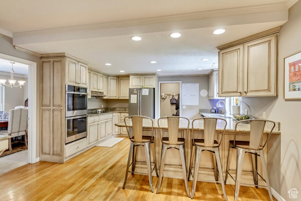 Kitchen featuring a peninsula, under cabinet range hood, ornamental molding, and stainless steel appliances