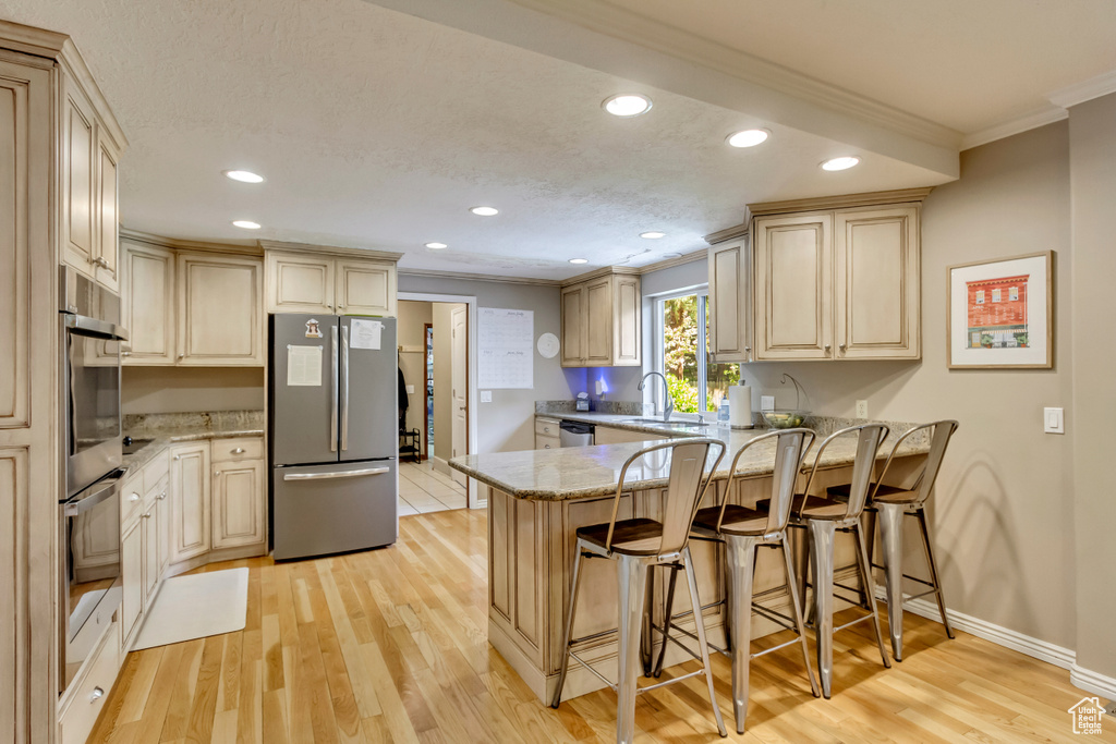 Kitchen with stainless steel appliances, a sink, light wood-style floors, crown molding, and a peninsula