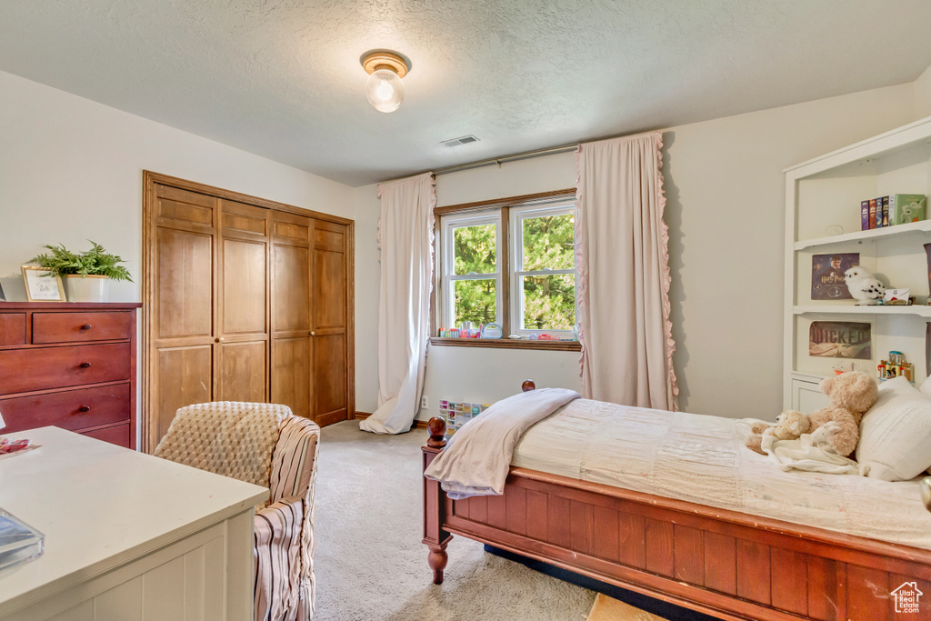Bedroom featuring light colored carpet, a textured ceiling, visible vents, and a closet