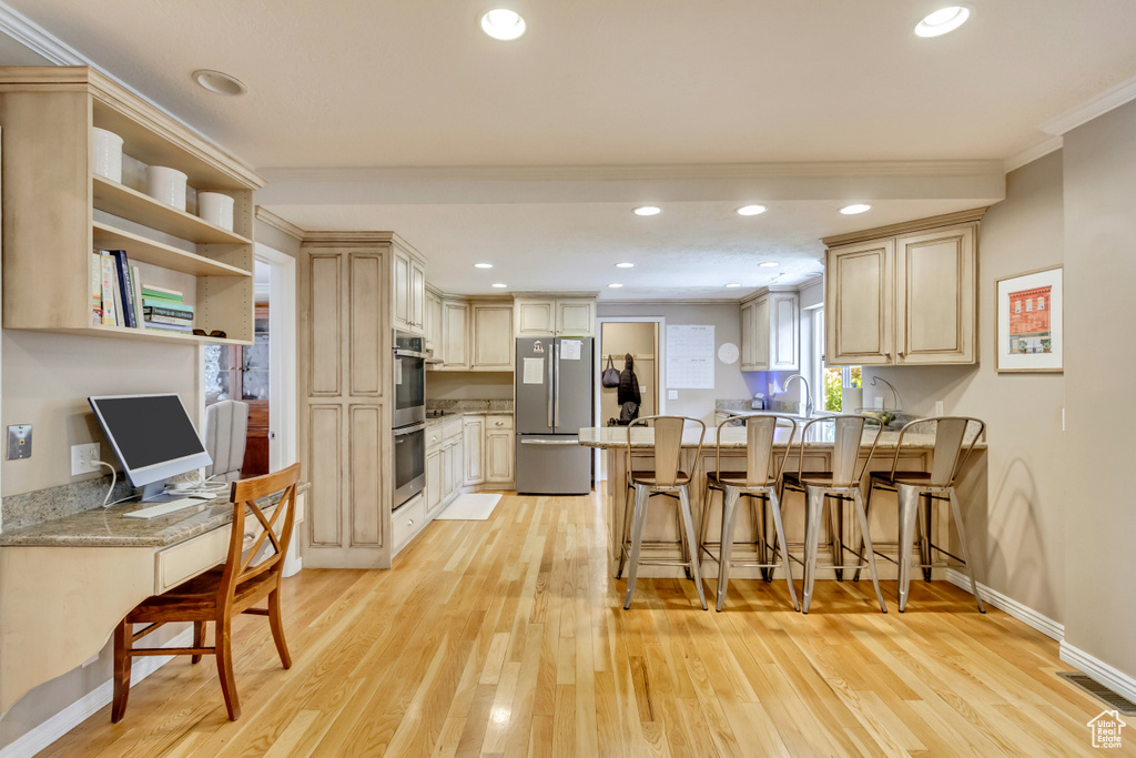Kitchen with ornamental molding, a peninsula, appliances with stainless steel finishes, and light wood finished floors