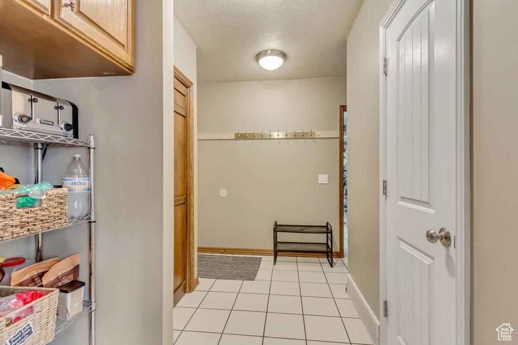 Doorway to outside featuring baseboards, a textured ceiling, and light tile patterned floors