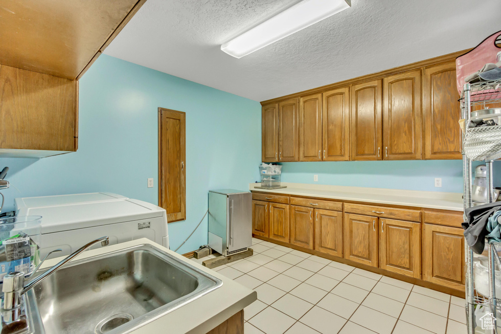 Laundry room featuring light tile patterned floors, a sink, washing machine and clothes dryer, cabinet space, and a textured ceiling