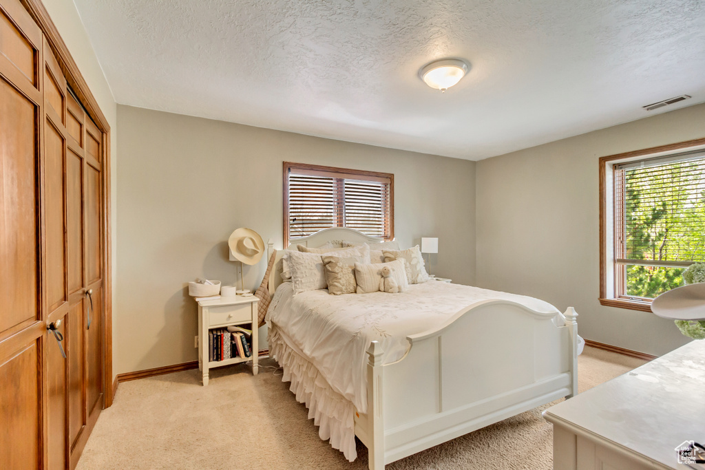 Bedroom with light carpet, baseboards, visible vents, and a textured ceiling