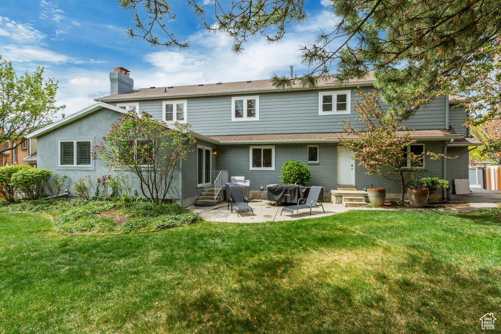 Back of property with a patio area, a chimney, a lawn, entry steps, and brick siding